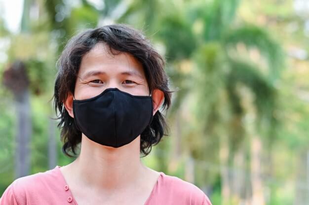 Seorang pria dengan kaos merah mudah mengenakan masker kain berwarna hitam